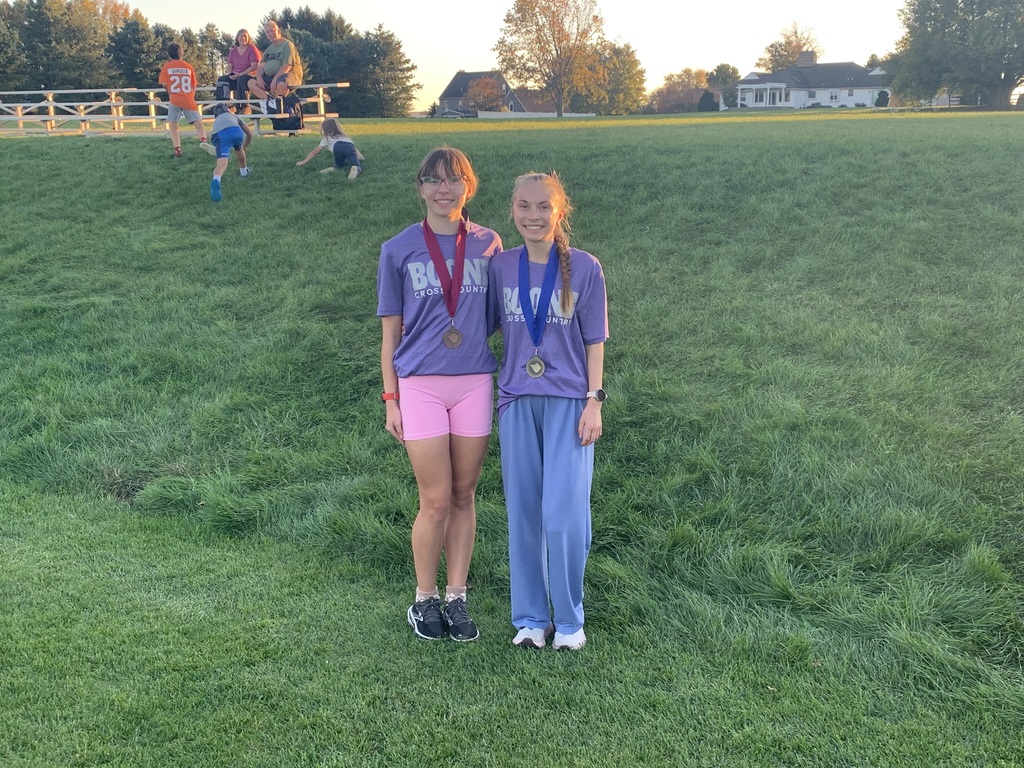 Two students standing next to a grass field wearing medals.