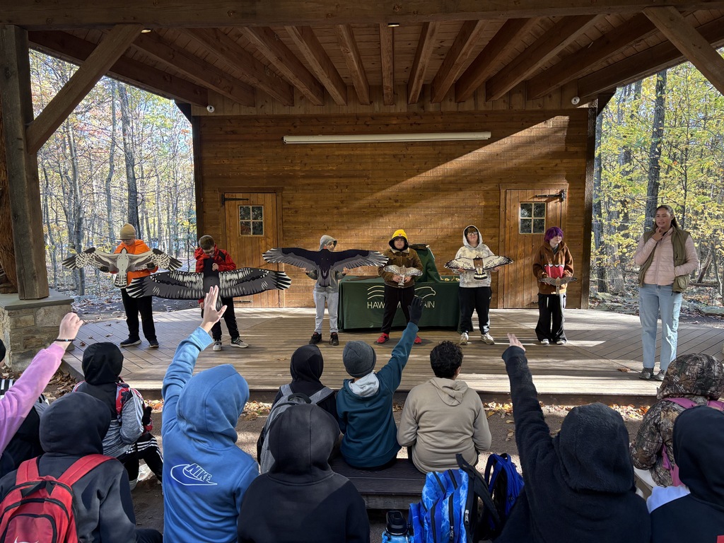 Students participate in a raptor presentation at Hawk Mountain, holding large bird-of-prey displays as classmates watch and raise their hands.