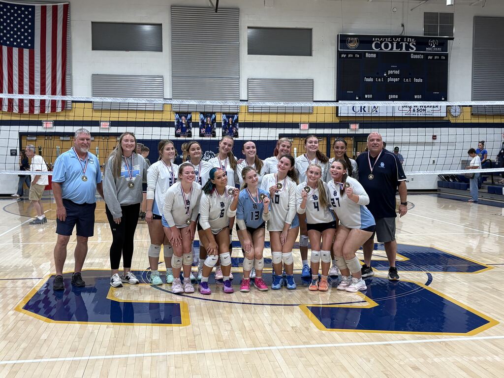 Picture of the girls volleyball team with their coaches standing in front of a volleyball net.