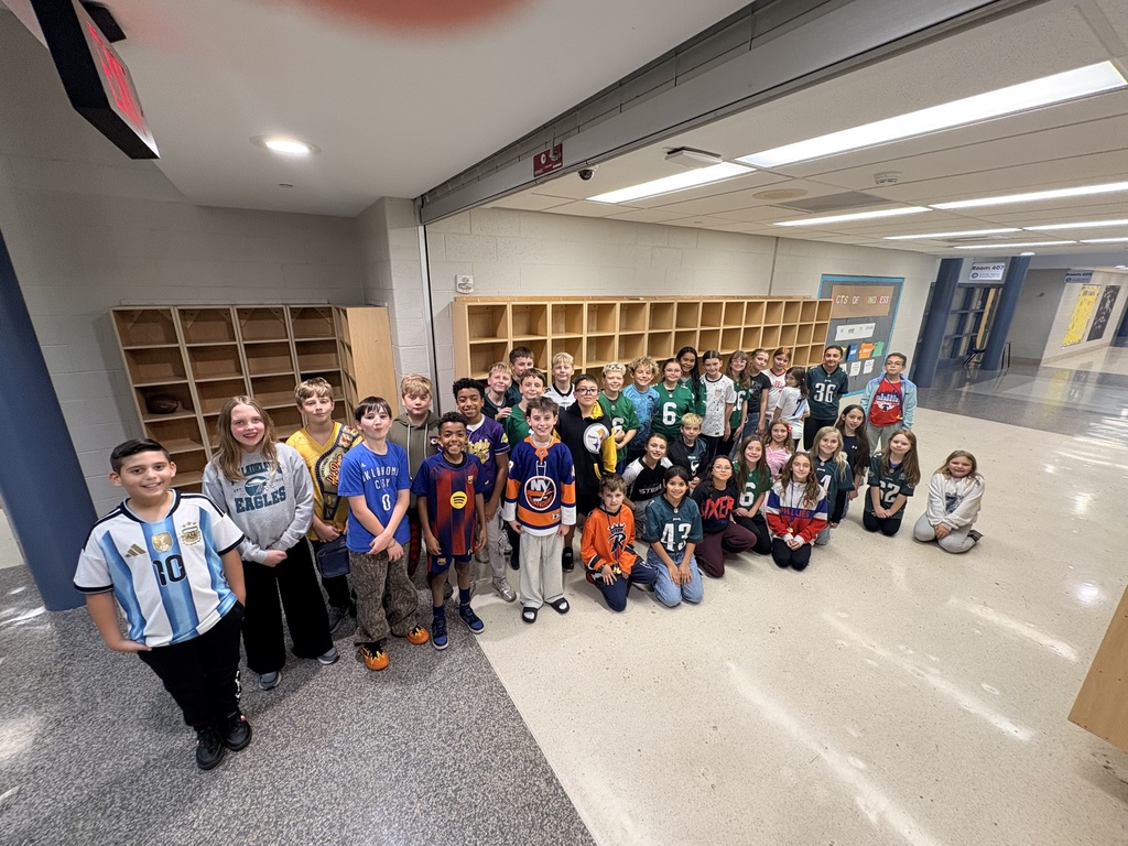 A group of 24 students pose in the hallway of the middle school wearing their team attire.