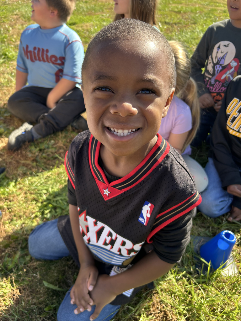 A student seated in the grass poses for the camera while wearing his Sixers jersey