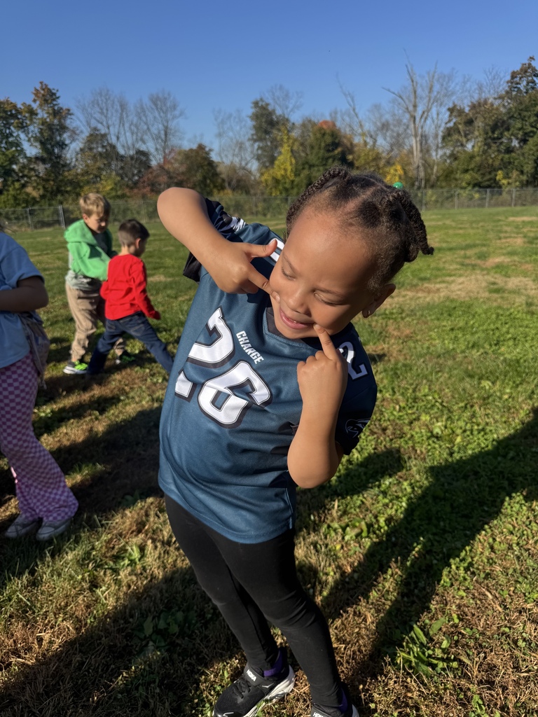 A smiling student (holding the corners of her mouth to accentuate her smile) wearing her Eagles jersey.