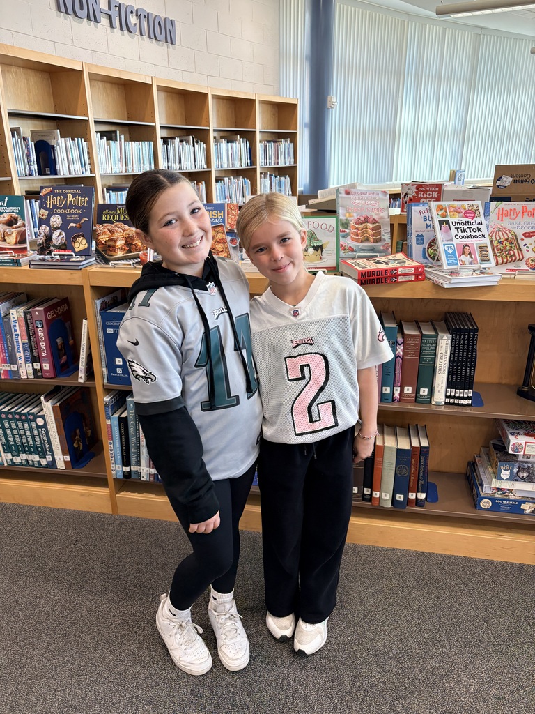 Two students wearing Eagles shirts pose for the camera in the middle school library.