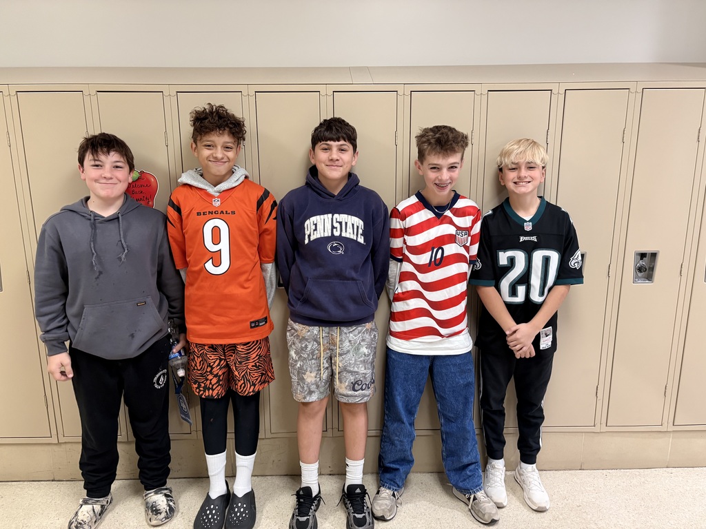 5 boys stand in front of lockers at the middle school wearing their team attire.
