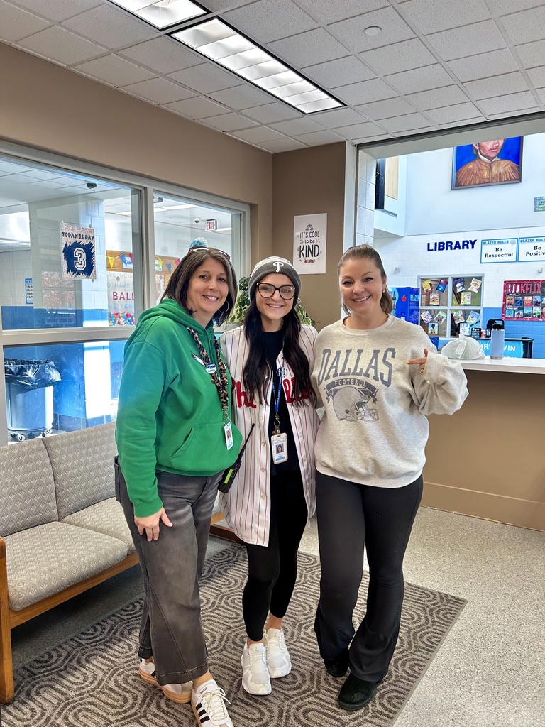 Three staff members wearing Eagles, Phillies and Dallas team attire pose for the camera in the office of the Intermediate Center