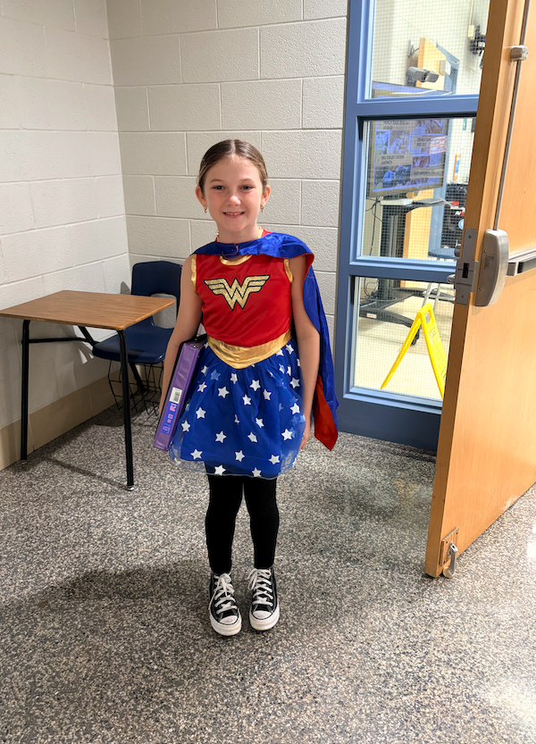 A student carrying a notebook stops outside the classroom door to show off her Wonder Woman costume