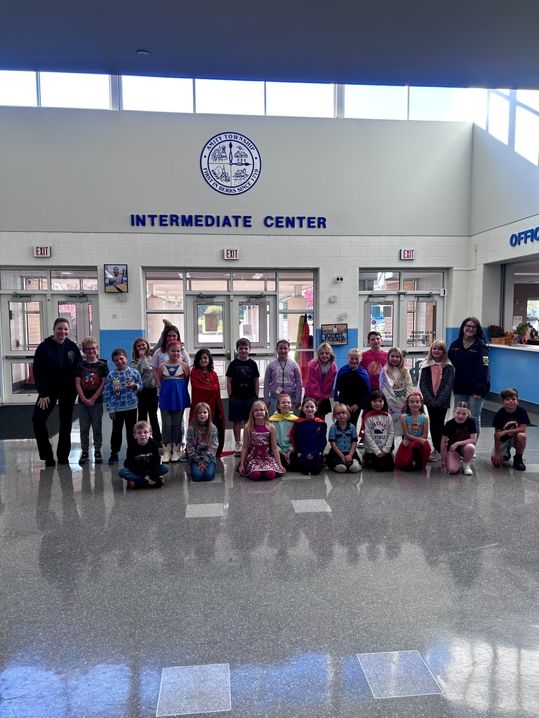 A group of 23 students along with two administrative assistants pose in the lobby of the Intermediate Center wearing their heroes costumes.