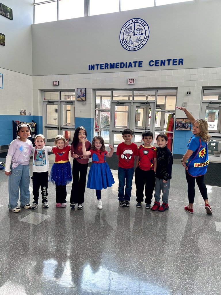 Mrs. Antolic strikes a Superman pose as she stands with her class who are all wearing superhero attire.