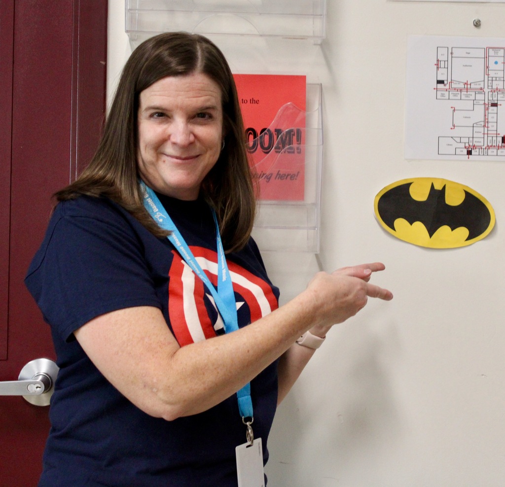 A teacher, wearing a Captain America T-shirt points to her Batman logo on the whiteboard