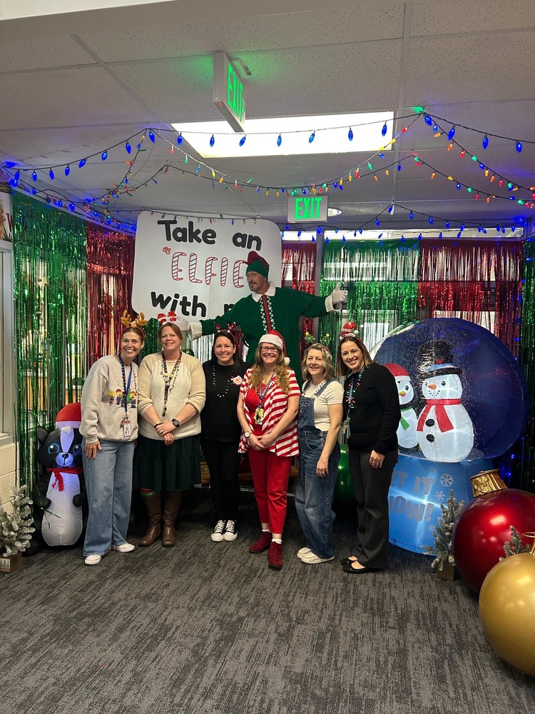 Office staff taking an "elfie" with Pinky the elf in front of the decorated doors.