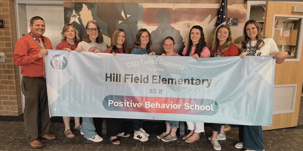 Teachers and administration are holding a banner that says, "DSD Tier Supports recognizes Hill Field Elementary as a Positive Behavior School."