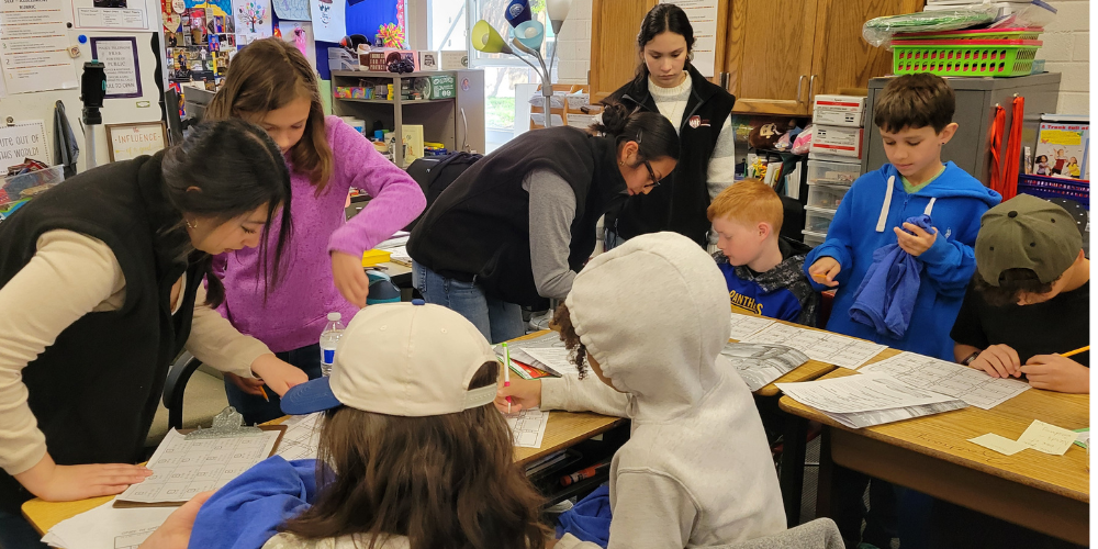Three high school students in the Latinos in Action program are working with six  5th grade boys and girls at their desks on math skills. 