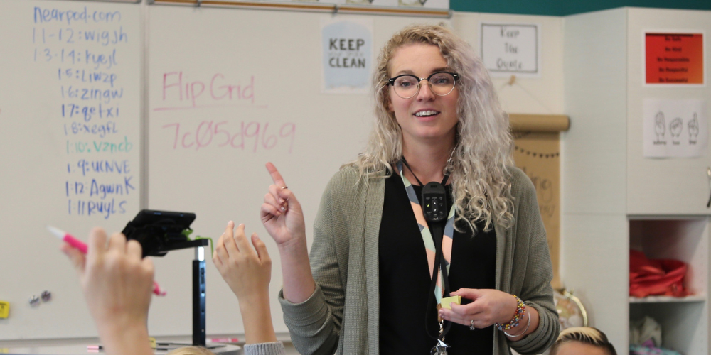 A teacher holding up her pointer finger while talking to her students.
