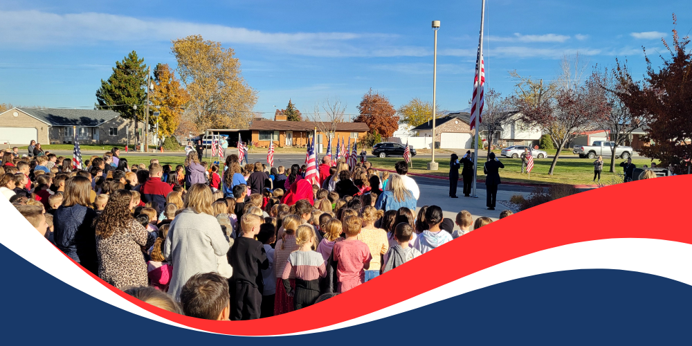 Students gather around an American Flag outside for a flag raising ceremony. 