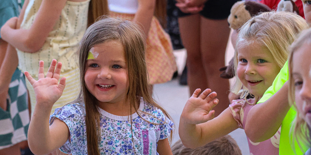 Two young students waving and smiling.