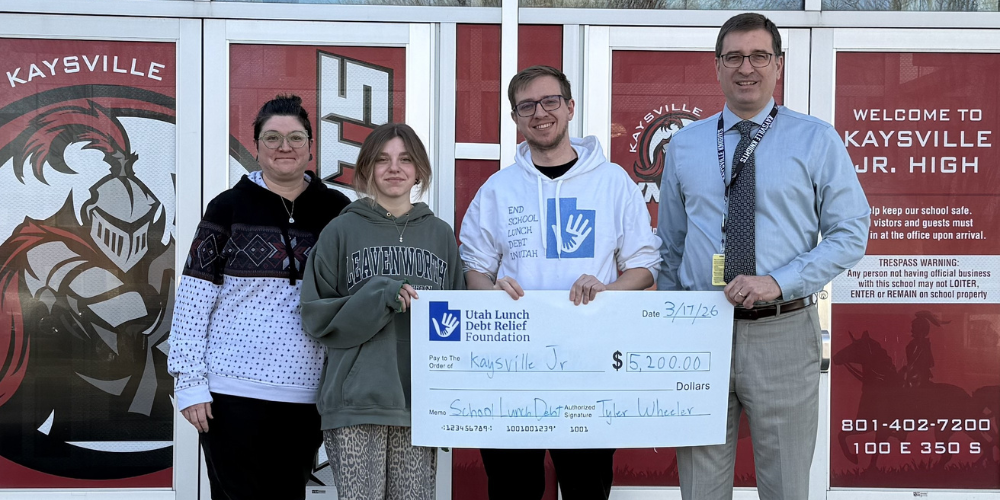 image of 4 people standing in front of kaysville junior high holding a check from utah lunch debt relief