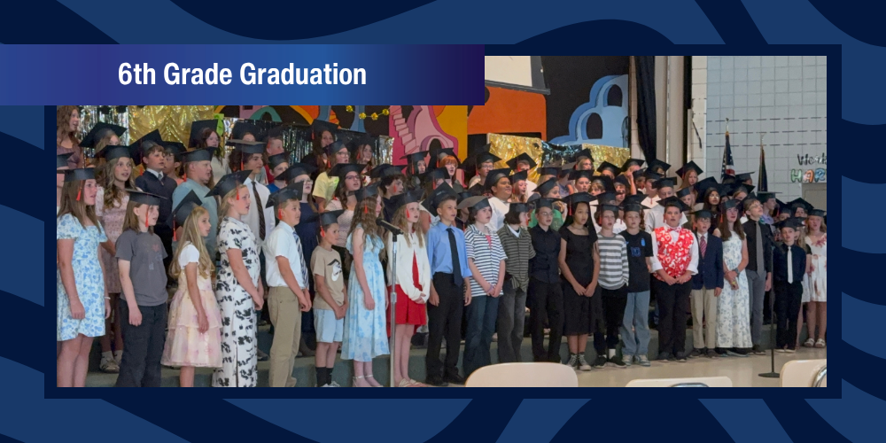 Students stand on stage wearing paper graduation hats.