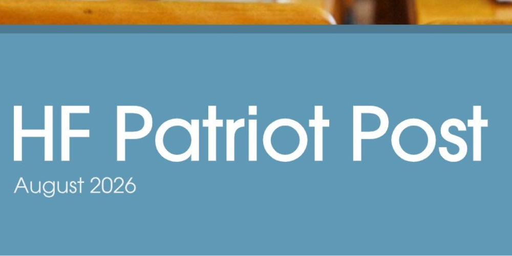 blue banner with the words HF Patriot Post August 2026.Behind the banner are wood desks with slates on them.
