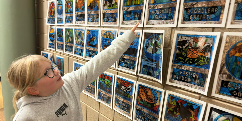 Student points to a wall with stained glass drawings to show which one is hers