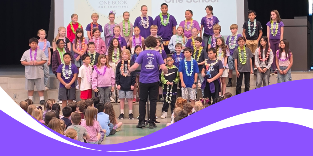 Bountiful Elementary school's choir gathered on stage during One Book, One Bountiful assembly in conjunction with Purple Up day,, framed by a purple wave graphic