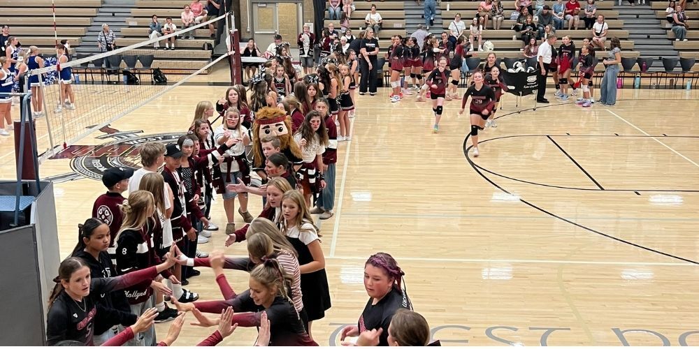 Two lines of girl volleyball players with their arms up so that players can run through the row when they are introduced.