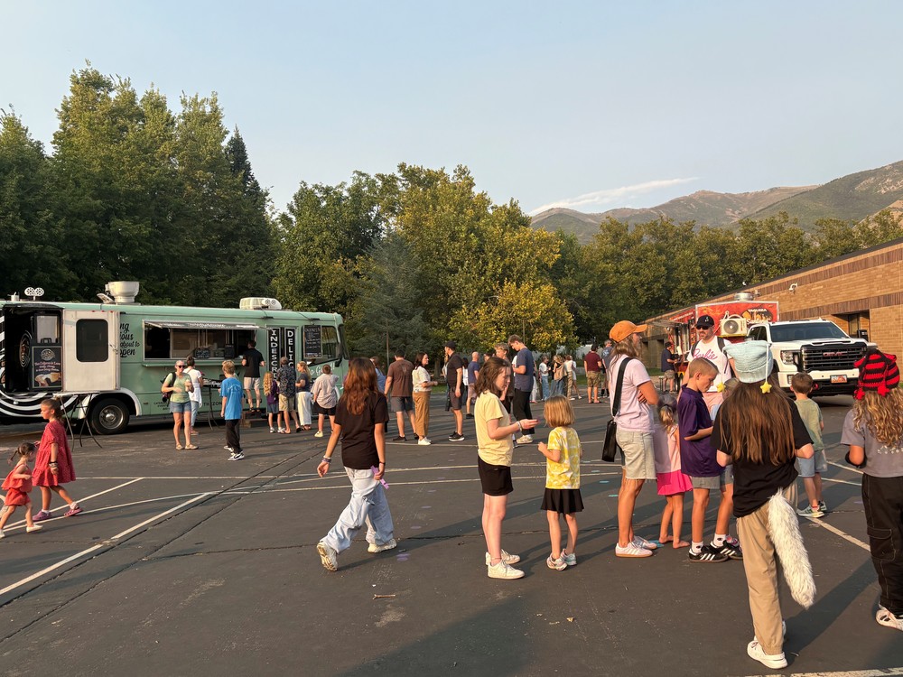 Crowd of people at an event outside with food trucks in the background.