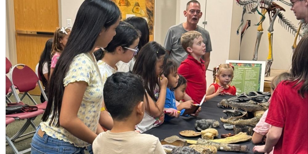 Students gather around a table of small dinosaur fossils and replicas.