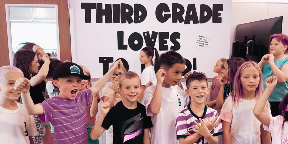 3rd Grade students cheering on their peers in front of a sign that says "Third Grade Loves to Read!"
