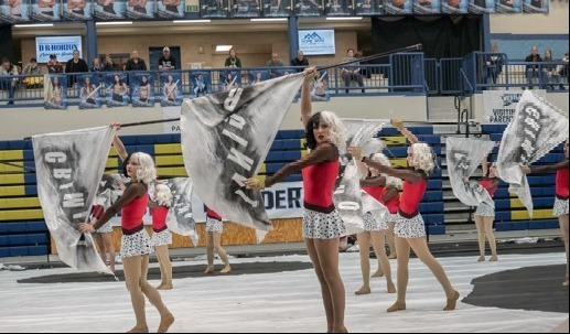 Girls holding flags in red and silver costumes wearing wigs that are half black and half white in a gym