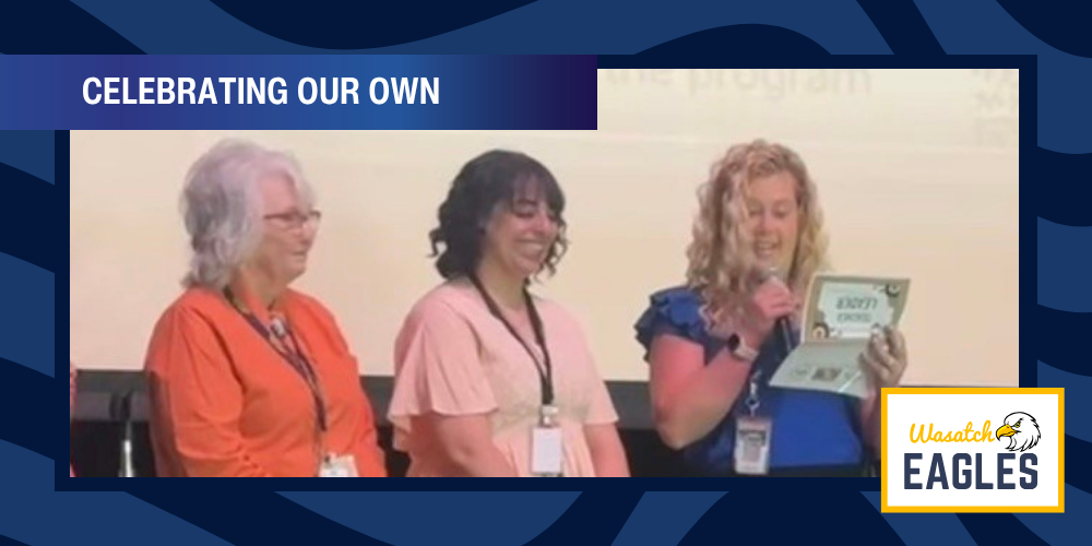 Three staff members stand on a stage during an event titled “CELEBRATING OUR OWN.” One person reads from a certificate into a microphone while the other two stand beside them. The slide design includes a blue patterned border and a “Wasatch Eagles” logo with an eagle graphic in the bottom right corner.