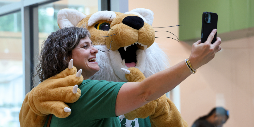 an adult selfies with a person in a bobcat costume. 