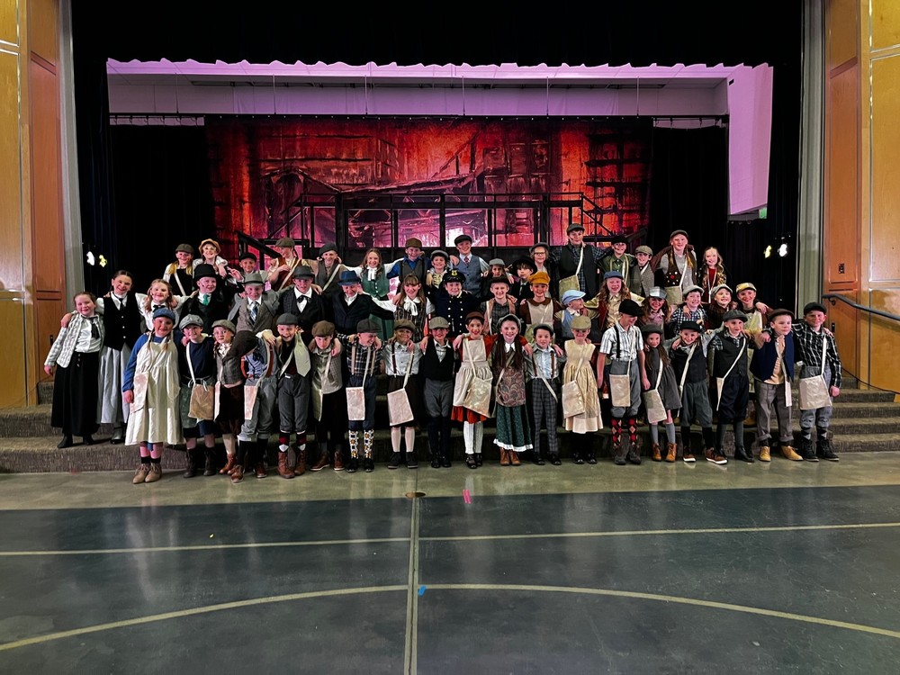 Students dressed as newsies for the school play standing on the stairs in front of the school play backdrop