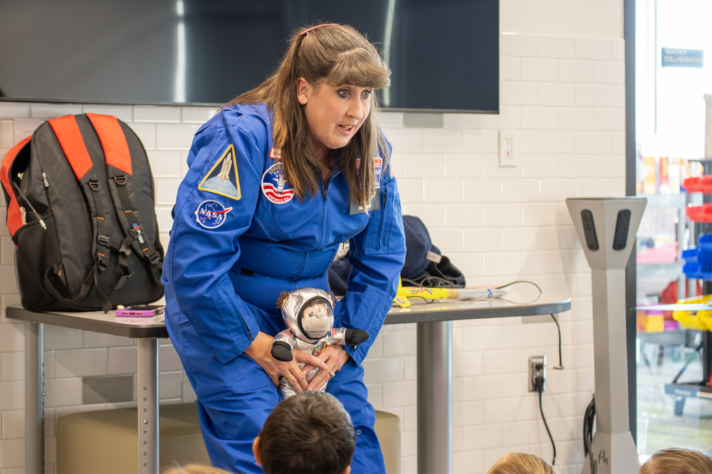 Mrs. Pandoff, in her space suit holding a stuffed monkey also dressed in its space suit discussing the solar system with first grade students 