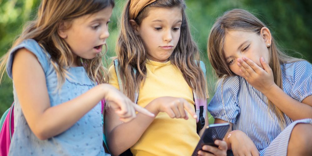 Girls looking at a cell phone with surprise.