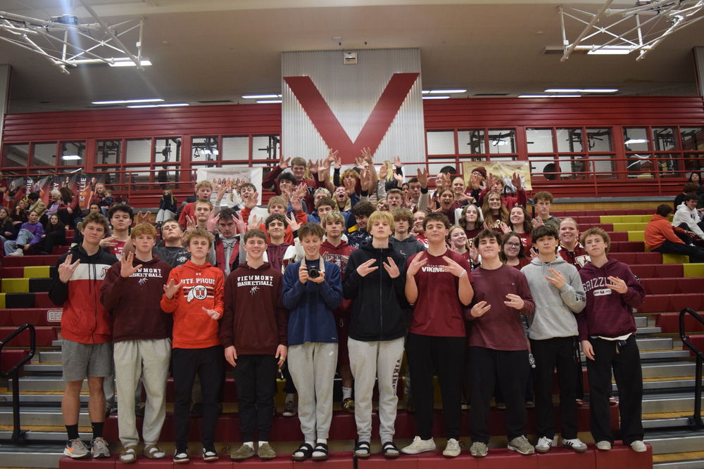 Large group of Viewmont High students on gym bleachers, many in maroon and red sweatshirts, smiling and flashing spirit hand signs beneath a giant “V” on the wall.