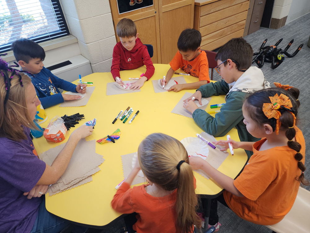 2nd grade students around a table doing a Halloween art activity.