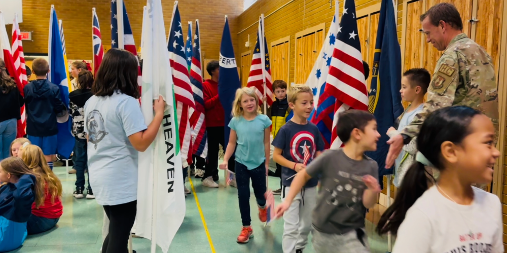 Image of students walking through trail of patriotic flags and high-fiving a veteran