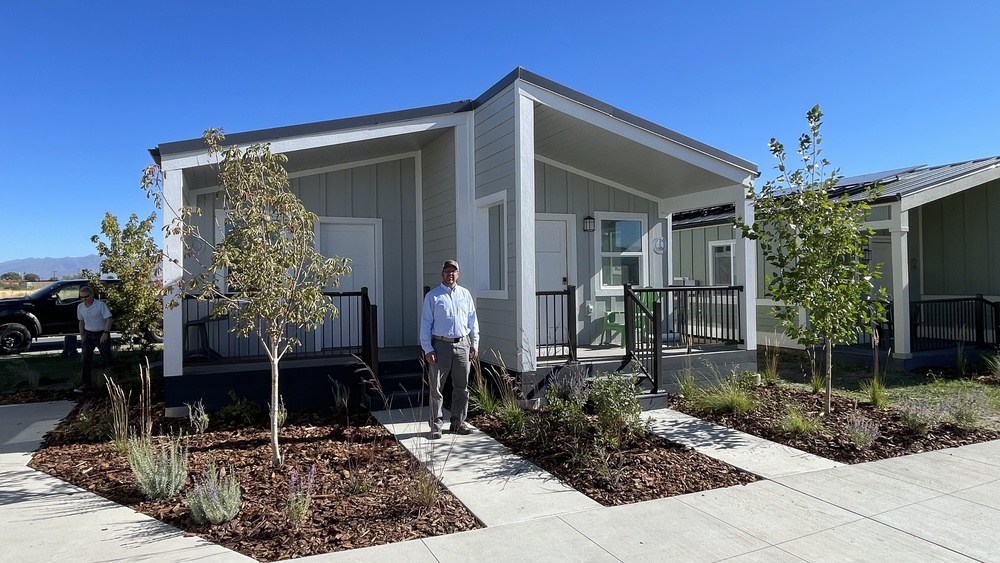 Jeremiah Allen, Construction  Management teacher, poses in front of home his students built at the "Other Side Village." 