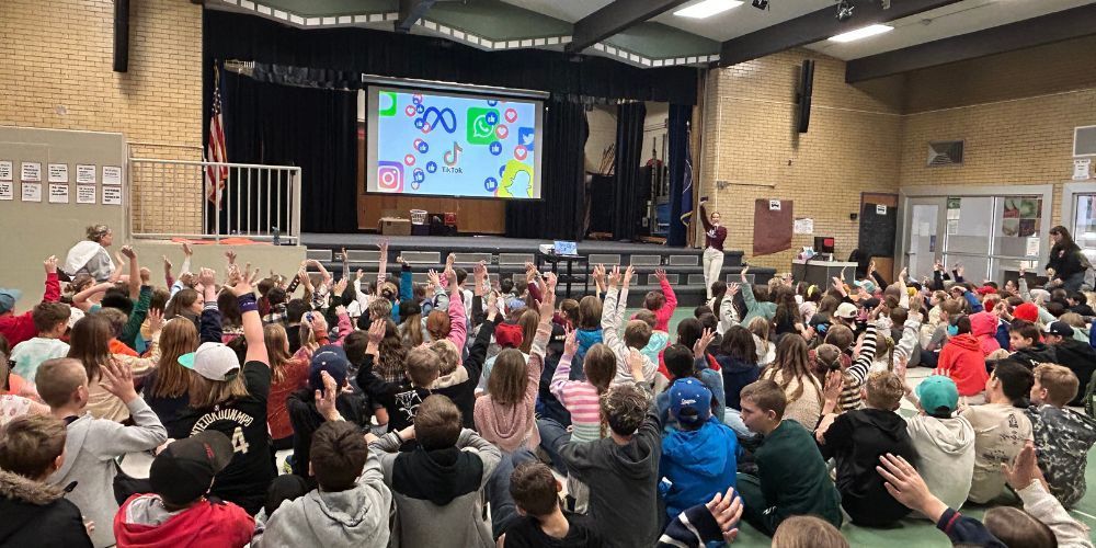 students in gym at an assembly with digital content on the screen 