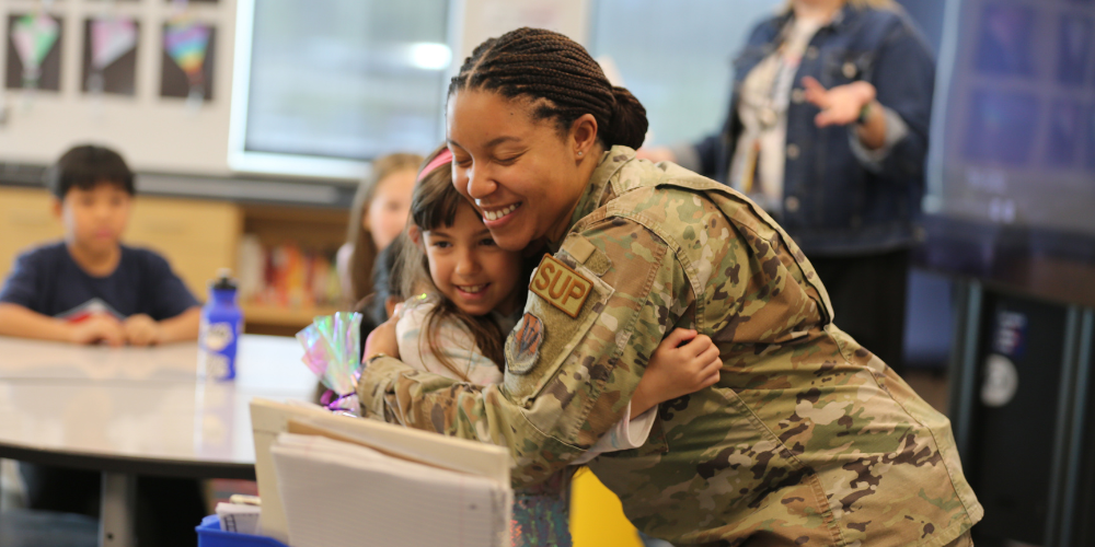 A military person hugging a student.