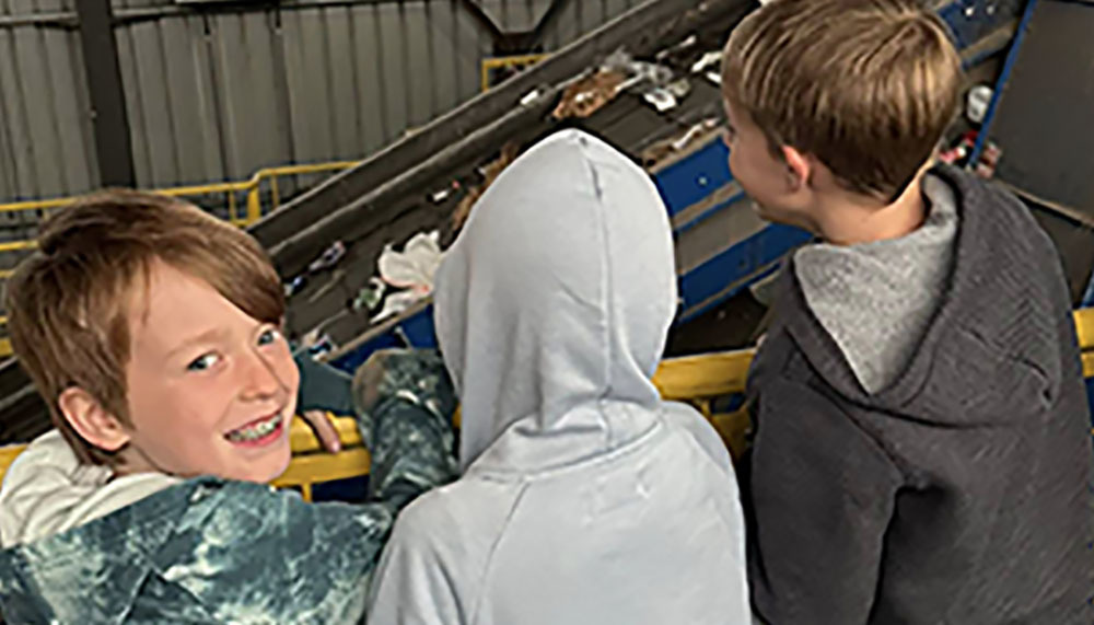 Three boys on a field trip to the waste treatment facility. They are watching a conveyor belt moving garbage. 