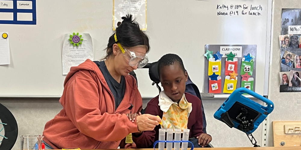 A teacher helping a student by dropping something into beakers. .