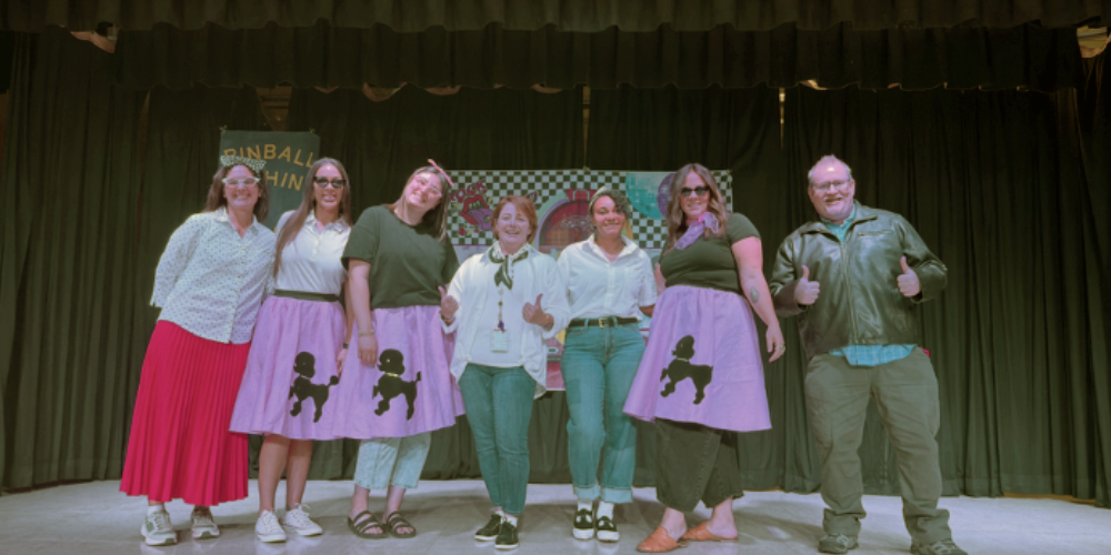 six teachers and one spouse dressed in 1950s clothing on the stage 