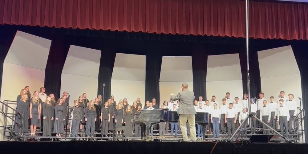 image of a choir standing on risers with a conductor leading the music