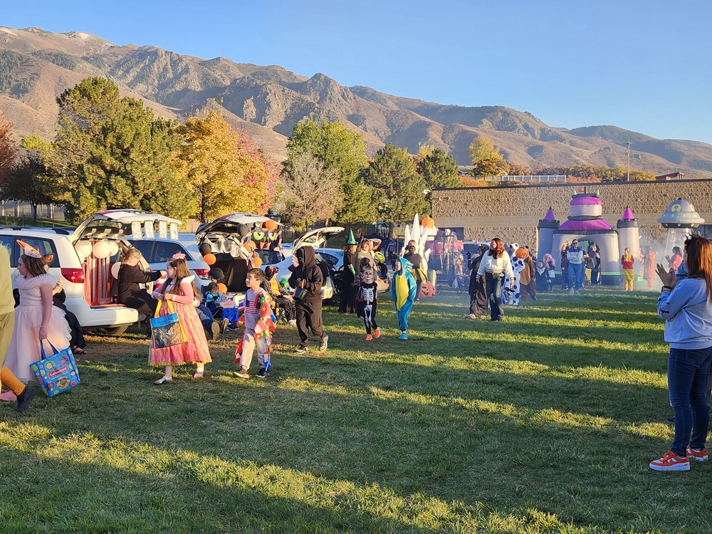 Students in costume parading through a line of cars on the playground with a blowup castle in the background
