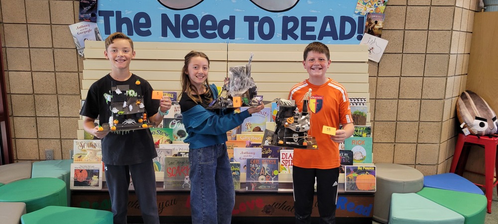 Students with Haunted Houses they created with paper and decorated with Halloween supplies.