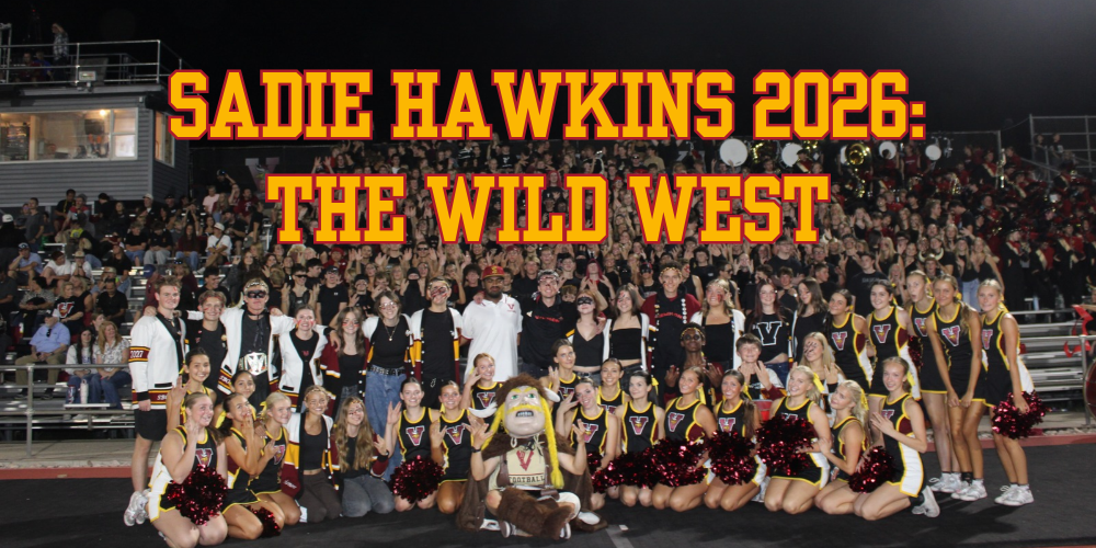Large group photo of Viewmont High School students, cheerleaders, football players, and staff posing together on a football field at night, with crowded stadium bleachers and a marching band in the background. Bold red and gold text reads “Sadie Hawkins 2026: The Wild West.”