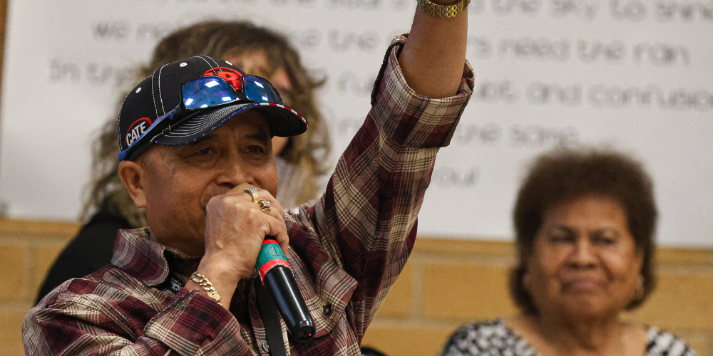 Chou talking into a microphone with his hand up.
