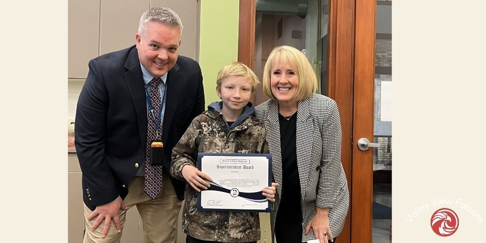 two adults, one male and one female, with boy in middle holding certificate for soup with the supe
