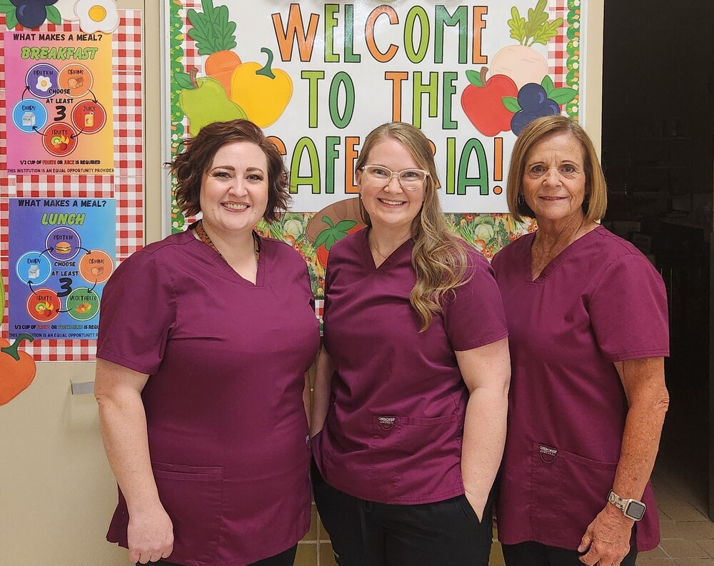 Lunch Ladies  standing in front of a welcome sign.